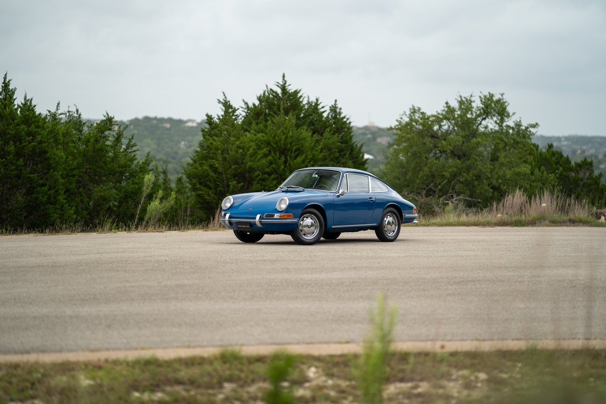 A blue 1965 Porsche 912 coupe with chrome trim and classic rims sits parked.