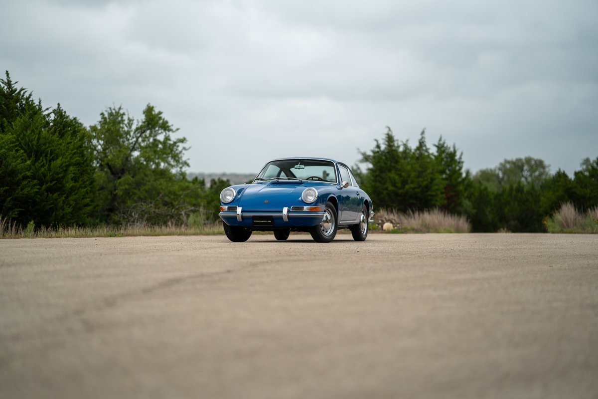 Blue 1965 Porsche 912 coupe, front view, on paved lot with trees.
