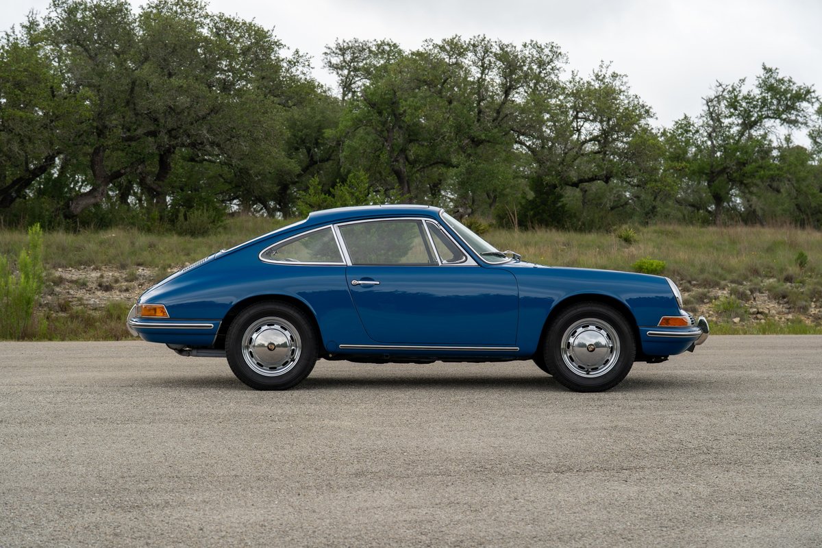 Blue 1965 Porsche 912 coupe with chrome hubcap rims parked on asphalt.