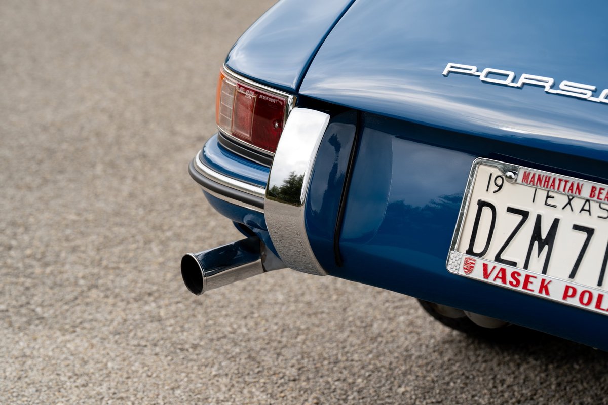 Detail of a vintage blue Porsche 912's rear bumper, exhaust pipe, and chrome trim.
