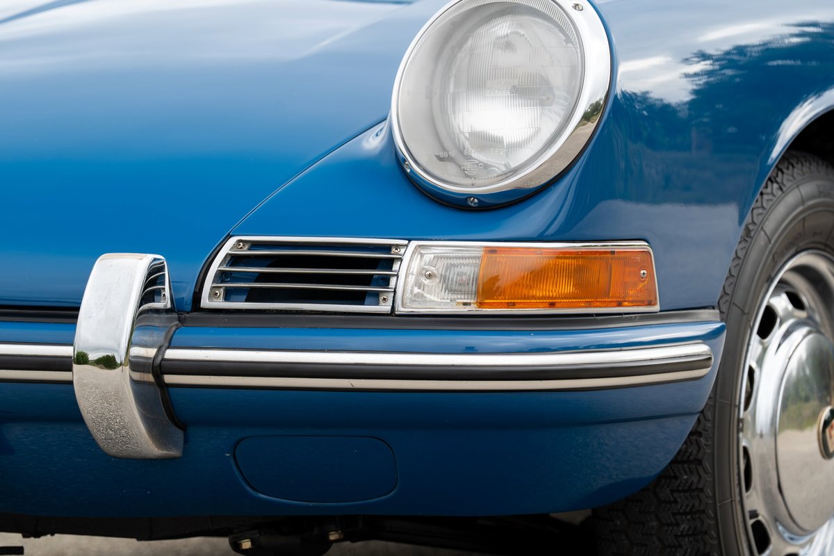 Close-up of a blue 1965 Porsche 912's front bumper, headlight, and chrome trim.