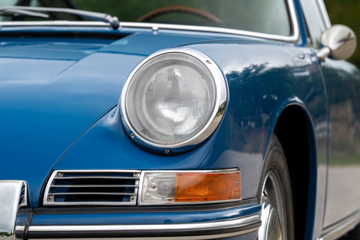 Close-up of a vintage blue Porsche 912's headlight and chrome trim.