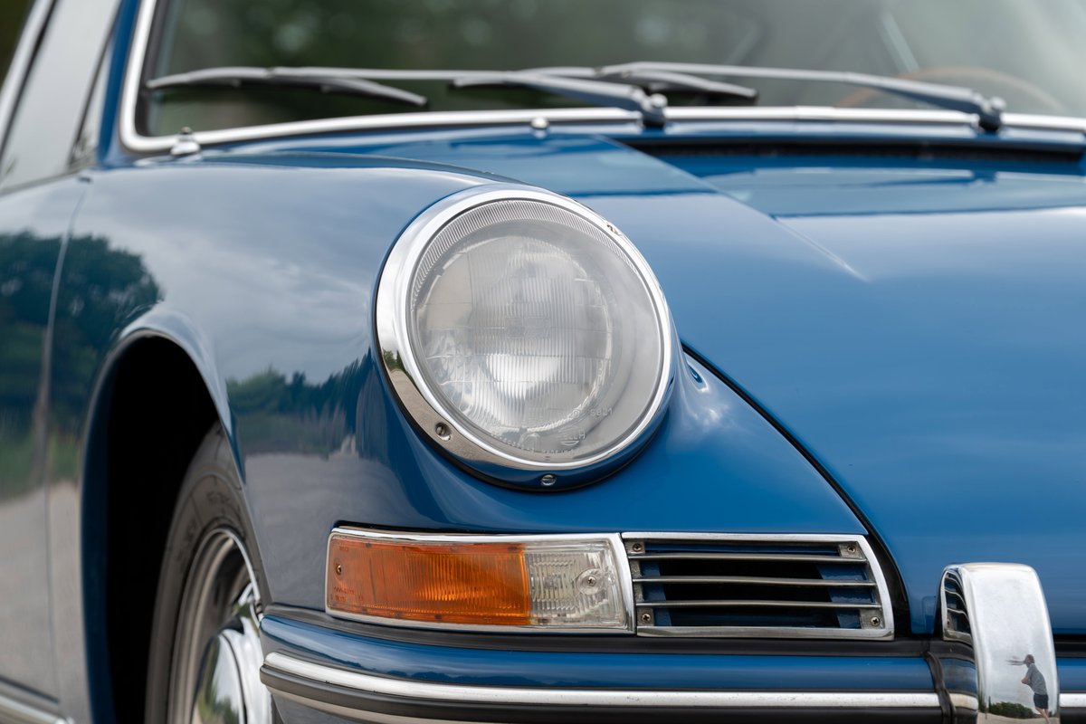 Close up of a blue 1965 Porsche 912 fender, showing chrome trim, headlight, and amber turn signal.