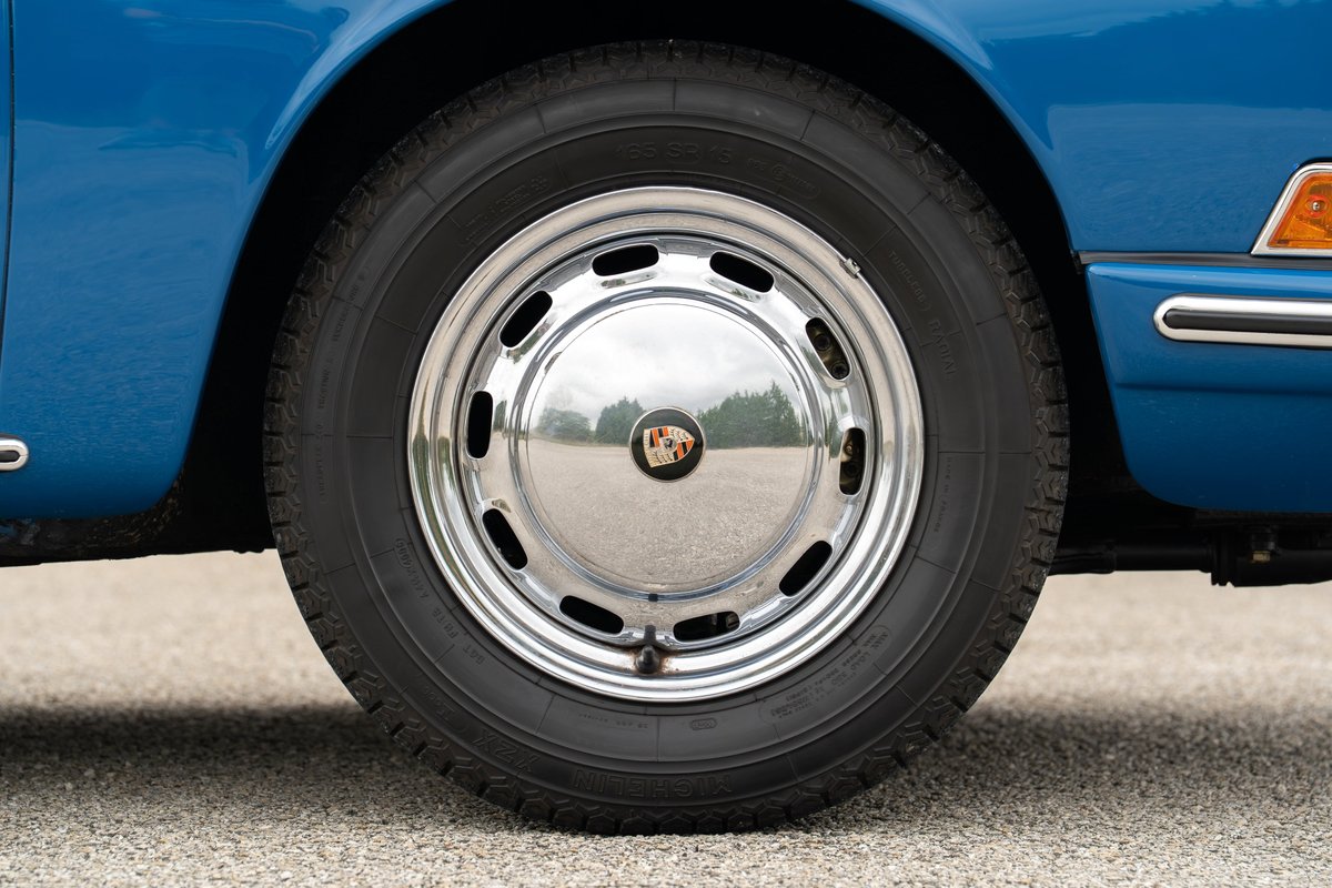Close up of a blue 1965 Porsche 912 wheel with chrome hubcap and Michelin tire.