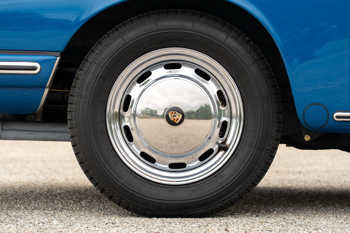 Close-up of a blue 1965 Porsche 912 wheel, featuring chrome rims and the Porsche crest.