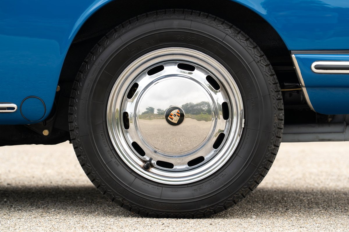 Close-up of a blue 1965 Porsche 912 with chrome hubcaps on its steel rims.