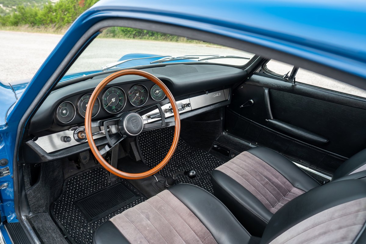 Interior of a 1965 blue Porsche 912, featuring a wood-rimmed steering wheel and classic gauges.