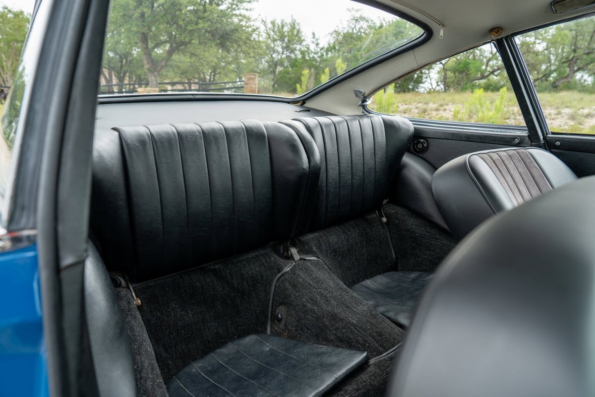 Interior view of a blue 1965 Porsche 912 with black leather rear seats and black carpeting.