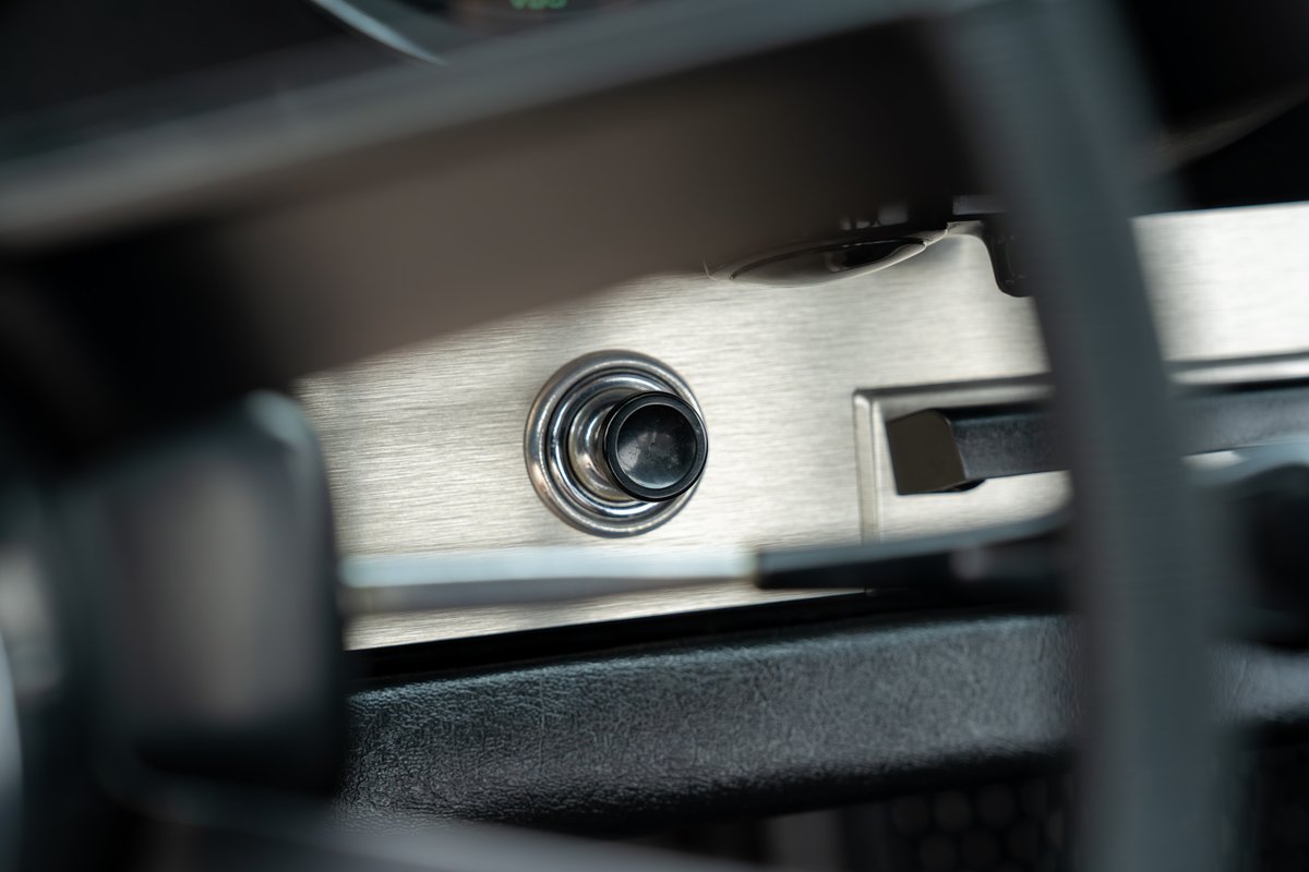 Close-up of a 1965 blue Porsche 912's brushed metal dash and toggle switch.