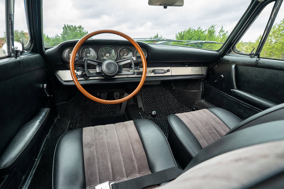 Interior of a 1965 Porsche 912 coupe with a wooden steering wheel and black seats.