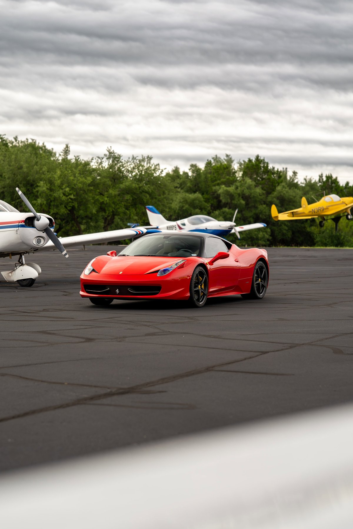 Red Ferrari 458 Italia with black rims on an asphalt runway with airplanes in the background.