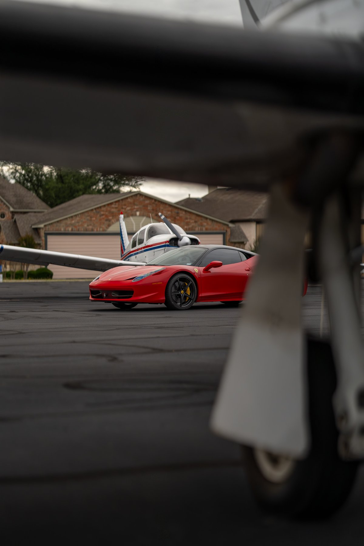 Red Ferrari 458 Italia with black trim and rims parked on tarmac next to a small airplane.