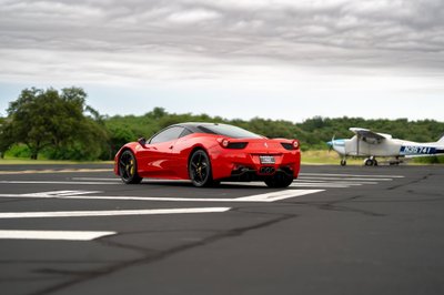 Red Ferrari 458 Italia on tarmac, black rims, dark tinted windows.