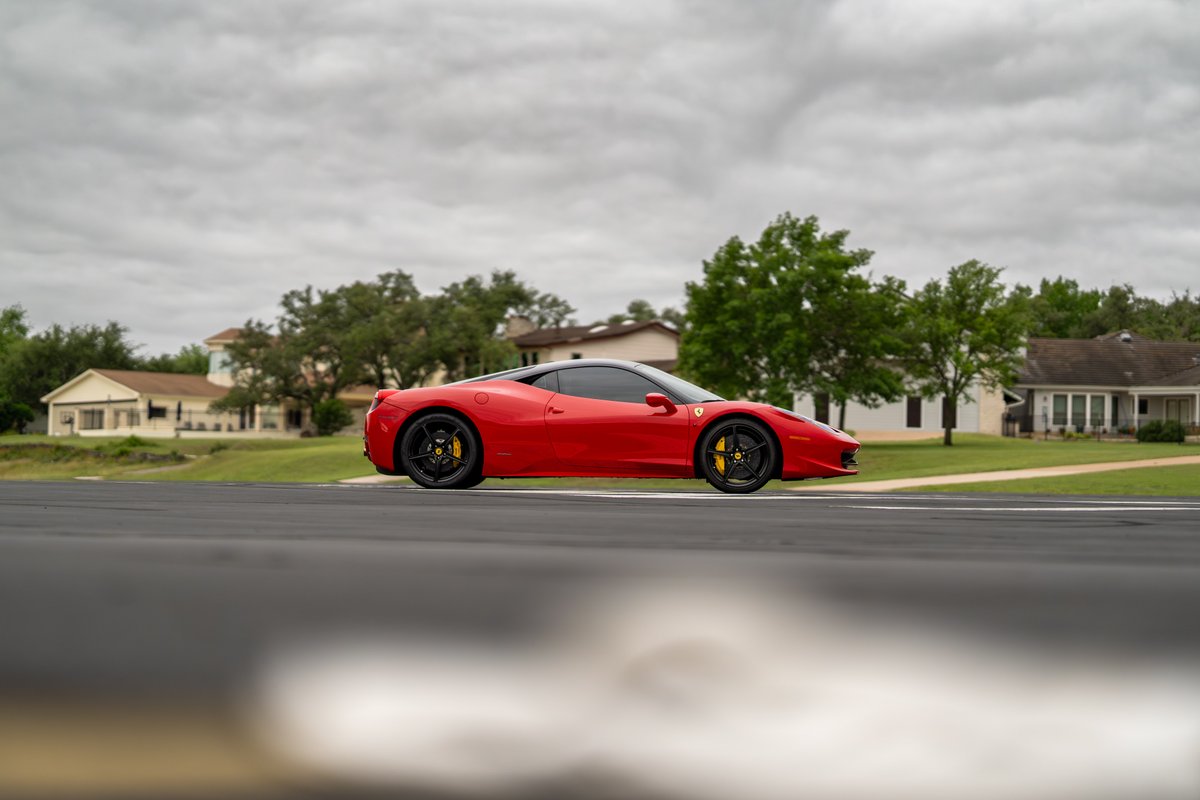 Red Ferrari 458 Italia with black rims and yellow brake calipers on a track.
