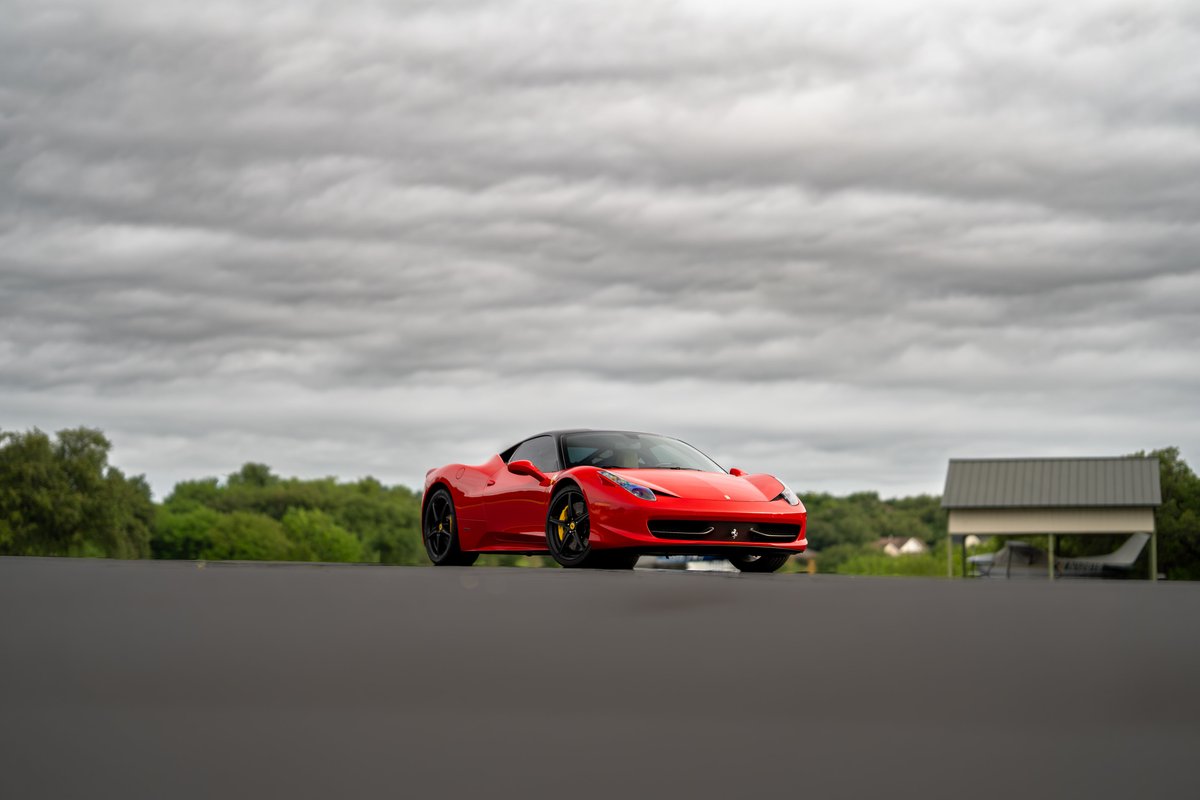 A red Ferrari 458 Italia with black roof and yellow brake calipers parked outdoors.
