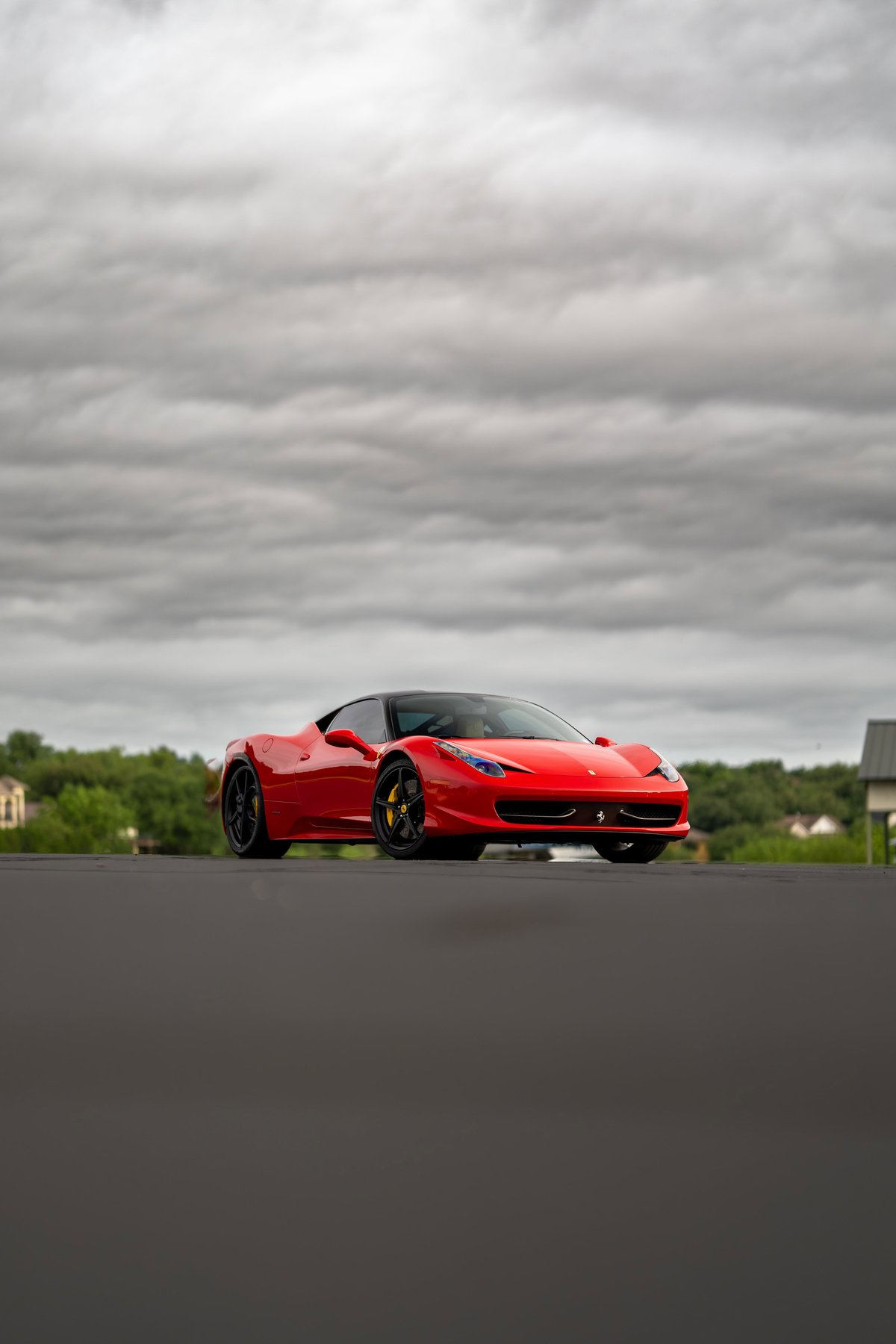 Red Ferrari 458 Italia with black rims and yellow brake calipers, parked under a cloudy sky.