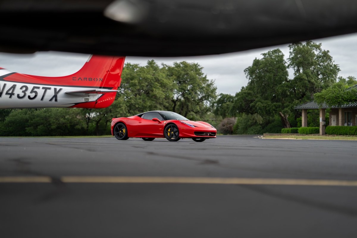 Red Ferrari 458 Italia on asphalt, near a plane. Black trim and yellow brake calipers.