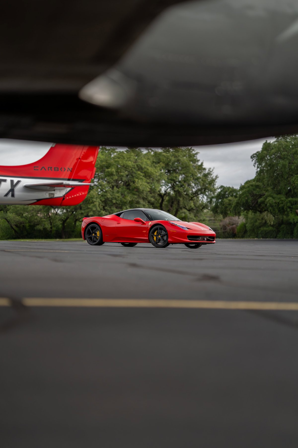 Red Ferrari 458 Italia with black rims and carbon fiber trim parked on tarmac.
