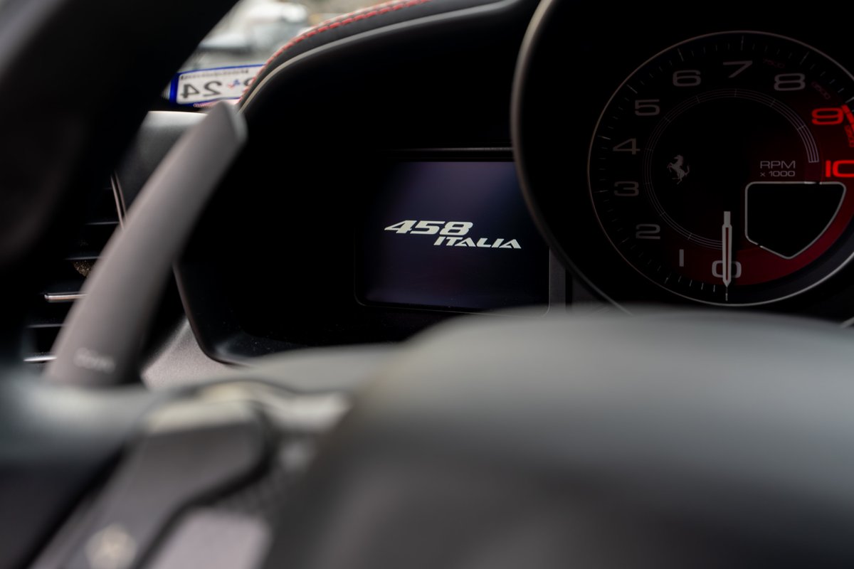 Interior shot of a Ferrari 458 Italia showing the digital display with "458 ITALIA" and the tachometer.
