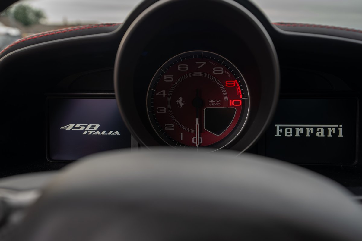 Closeup of a red 2015 Ferrari 458 Italia dashboard showing the tachometer, "458 ITALIA" and "Ferrari" badging.