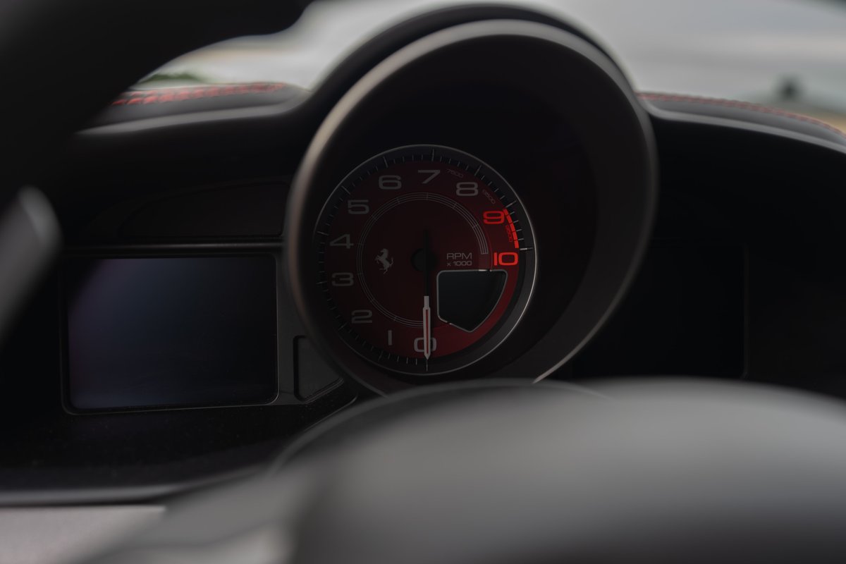 Close up of a red Ferrari 458 Italia's dashboard with a digital display and tachometer.