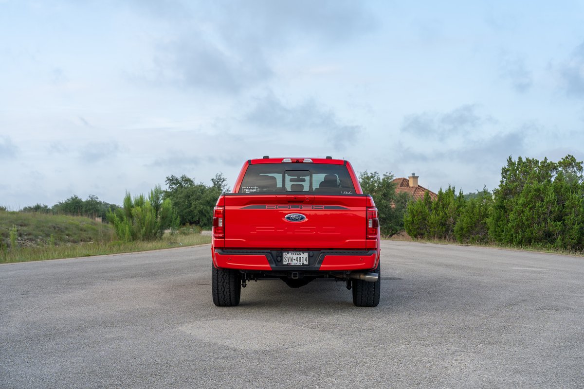 Red Ford F-150 Roush pickup truck parked on asphalt road, rear view, cloudy sky.