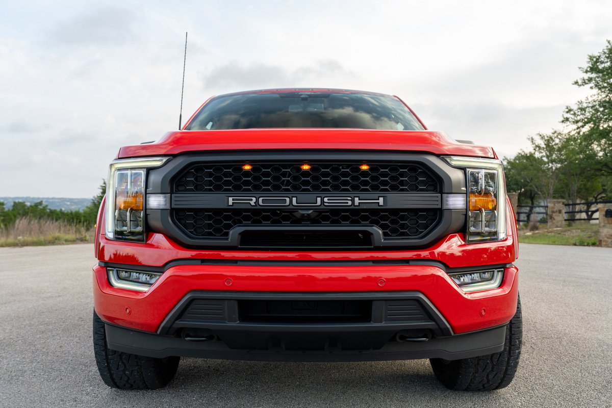 Front view of a red 2022 Ford F-150 ROUSH with a black honeycomb grille and orange accent lights.