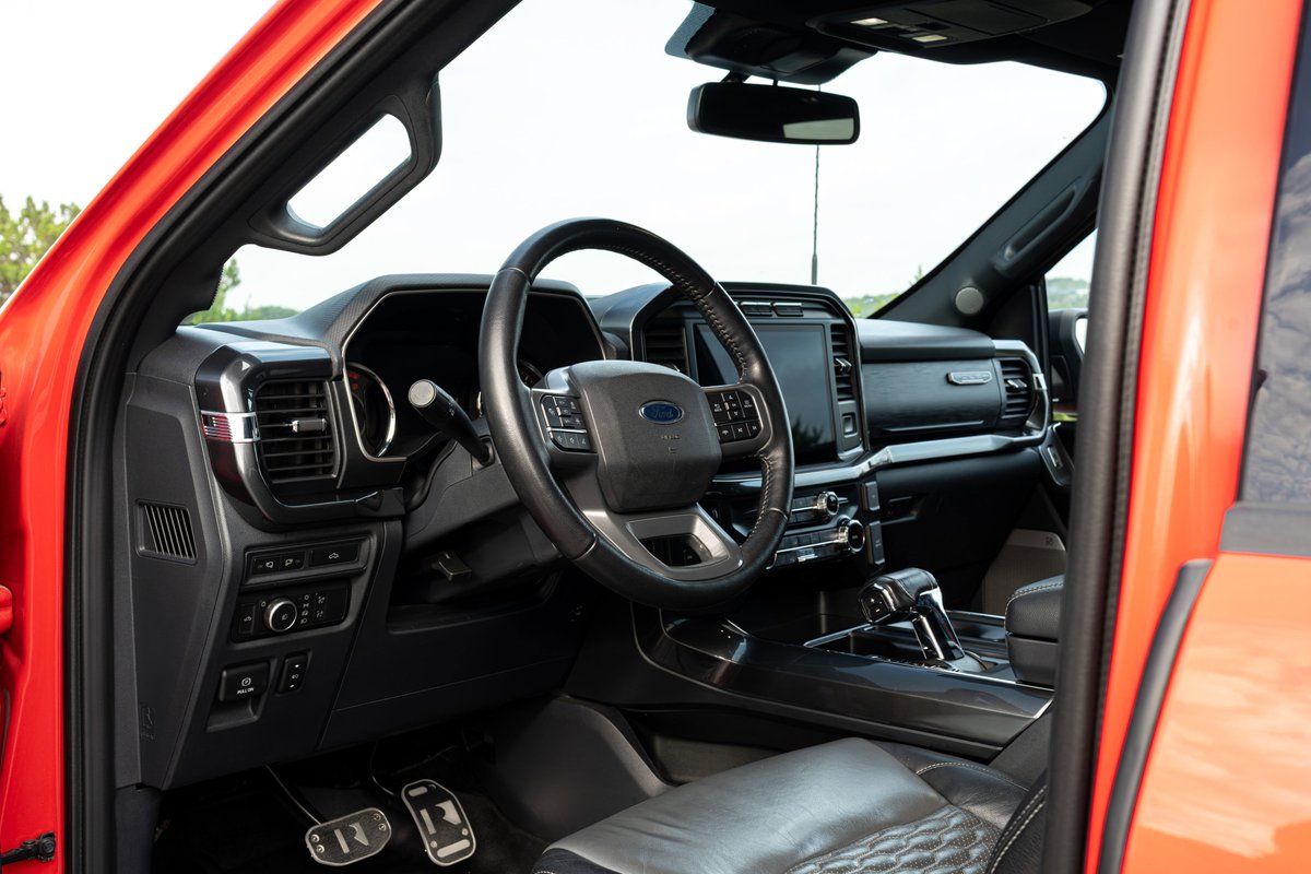 Interior of a red 2022 Ford F-150 Roush Raptor with a leather-stitched steering wheel and center console.