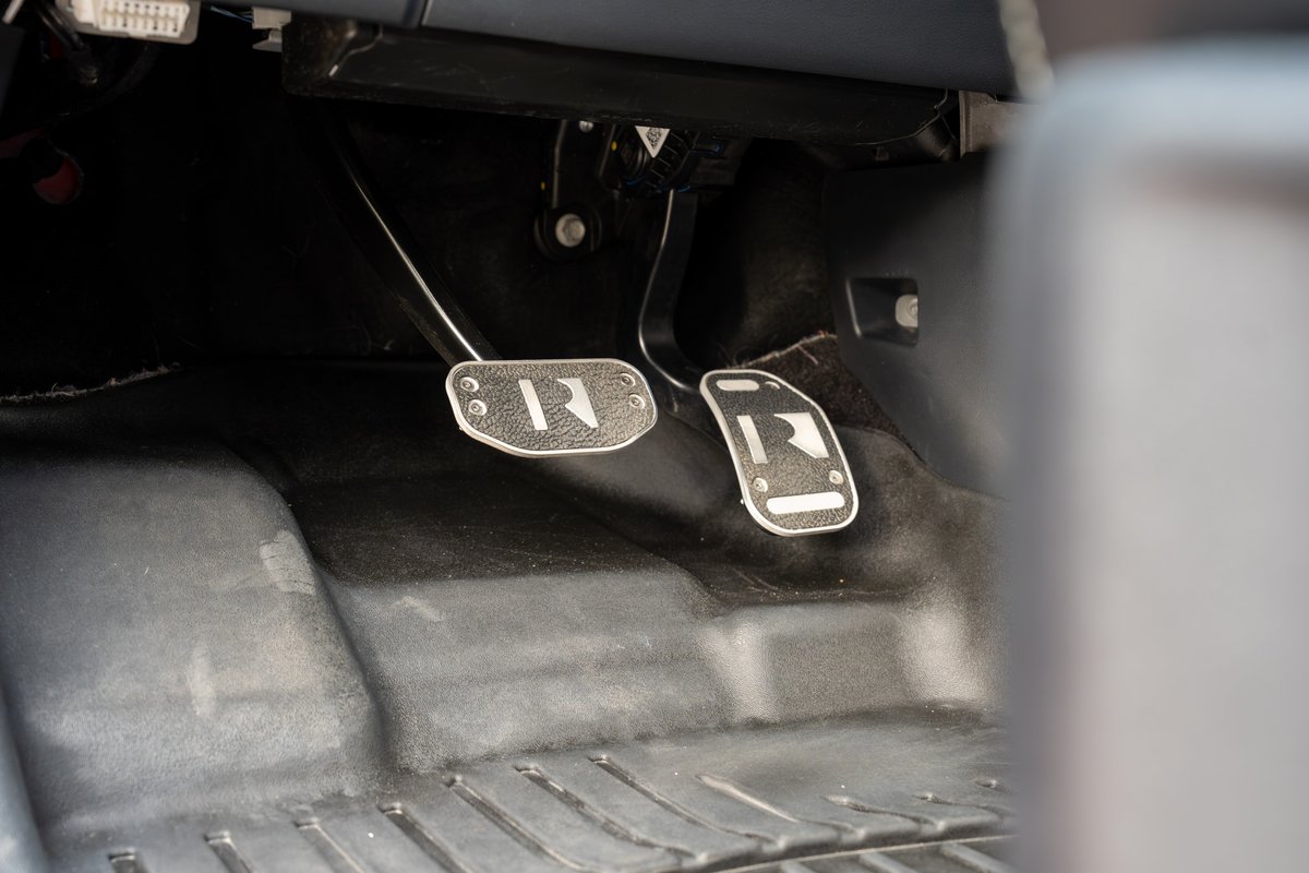 Close-up of the clutch and brake pedals in a red 2022 Ford F-150 Roush, featuring custom R-branded pedal covers.