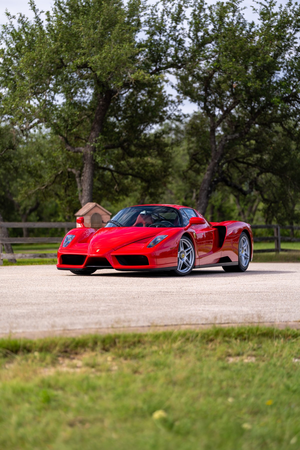 Rosso Corsa 2003 Ferrari Enzo driving on pavement with custom silver rims.