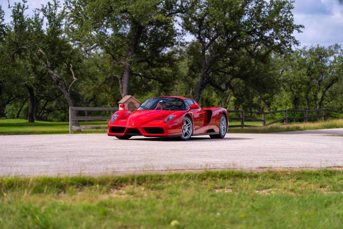 A red Ferrari Enzo with silver rims and dark trim is parked on a paved road.
