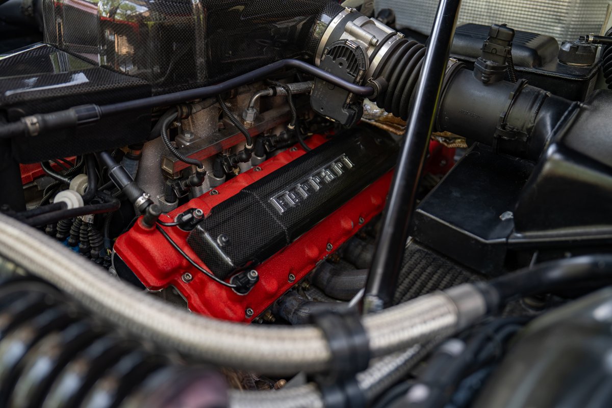Close-up of the Ferrari engine bay with red valve covers and carbon fiber trim.