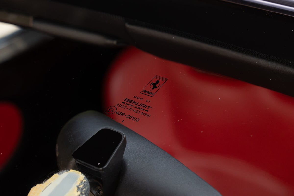 Ferrari Enzo windshield with Sekurit branding and Prancing Horse logo, Rosso Corsa interior visible.