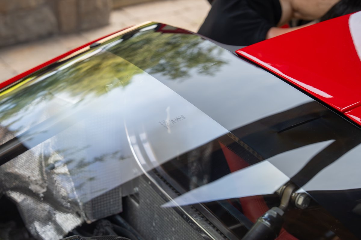 Closeup of a red 2003 Ferrari Enzo windshield and red body trim. Reflections show trees.