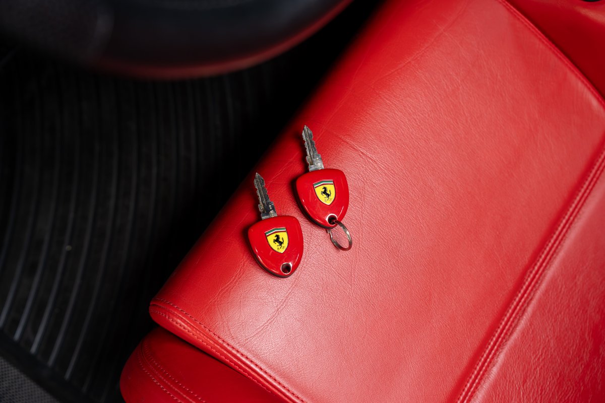 Two red Ferrari Enzo keys with prancing horse logo on red leather seat.