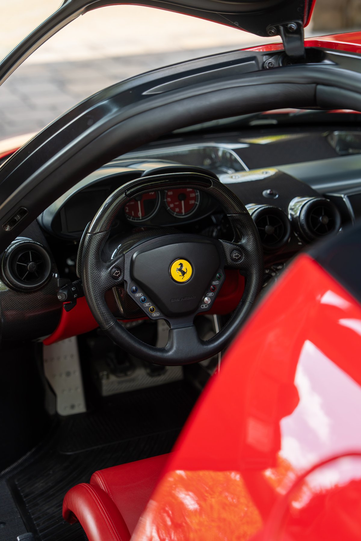 Rosso Corsa Ferrari Enzo interior with carbon fiber steering wheel and red leather seats.