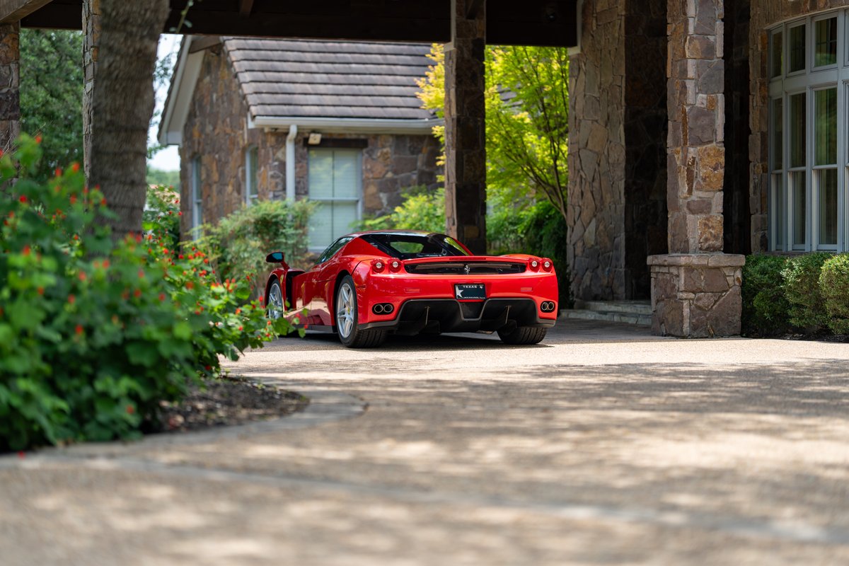 Red 2003 Ferrari Enzo with silver rims, parked in front of a stone house.