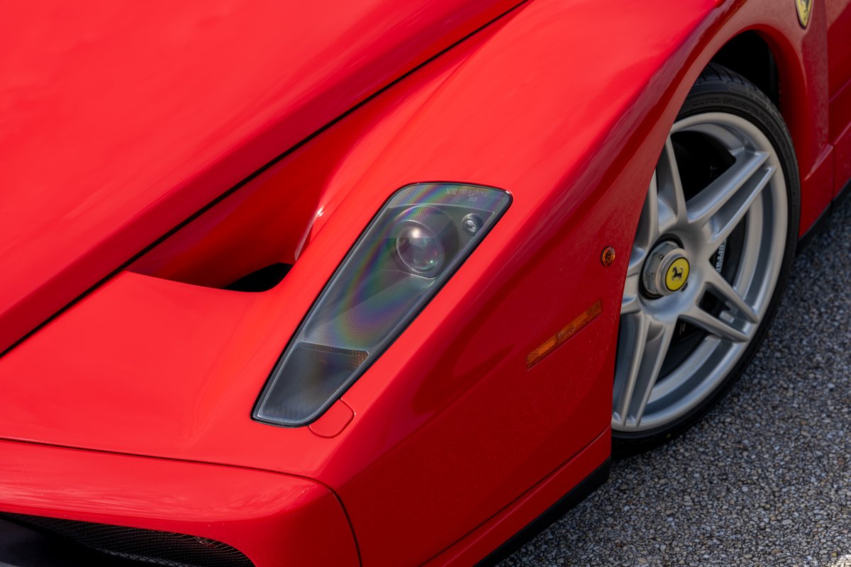 Close up of a red Ferrari Enzo with silver five-spoke rims and tinted headlights.