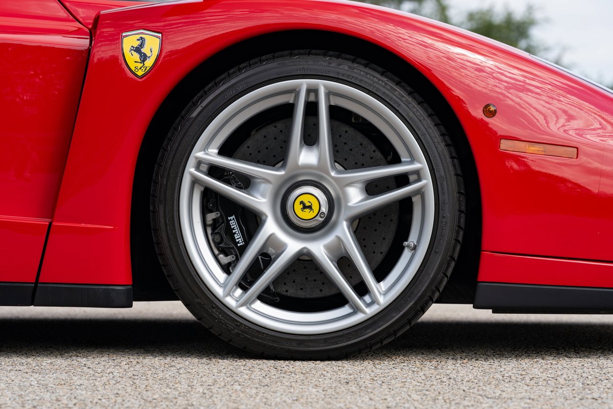 Close-up of a Rosso Corsa Ferrari Enzo wheel and fender with yellow Ferrari emblem.