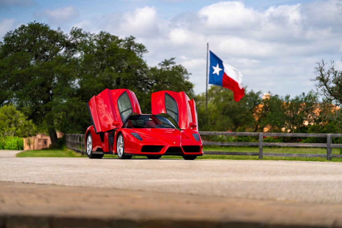 Red 2003 Ferrari Enzo with dihedral doors open and silver rims, Texas flag in background.
