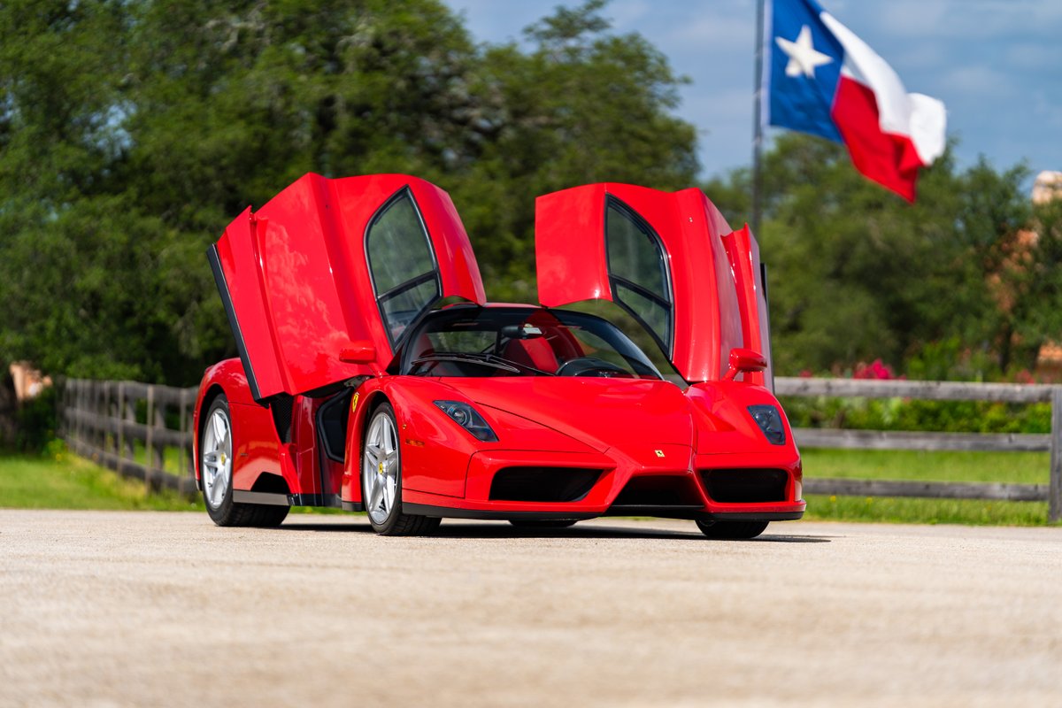 Red 2003 Ferrari Enzo with butterfly doors open, silver rims, Texas flag backdrop.