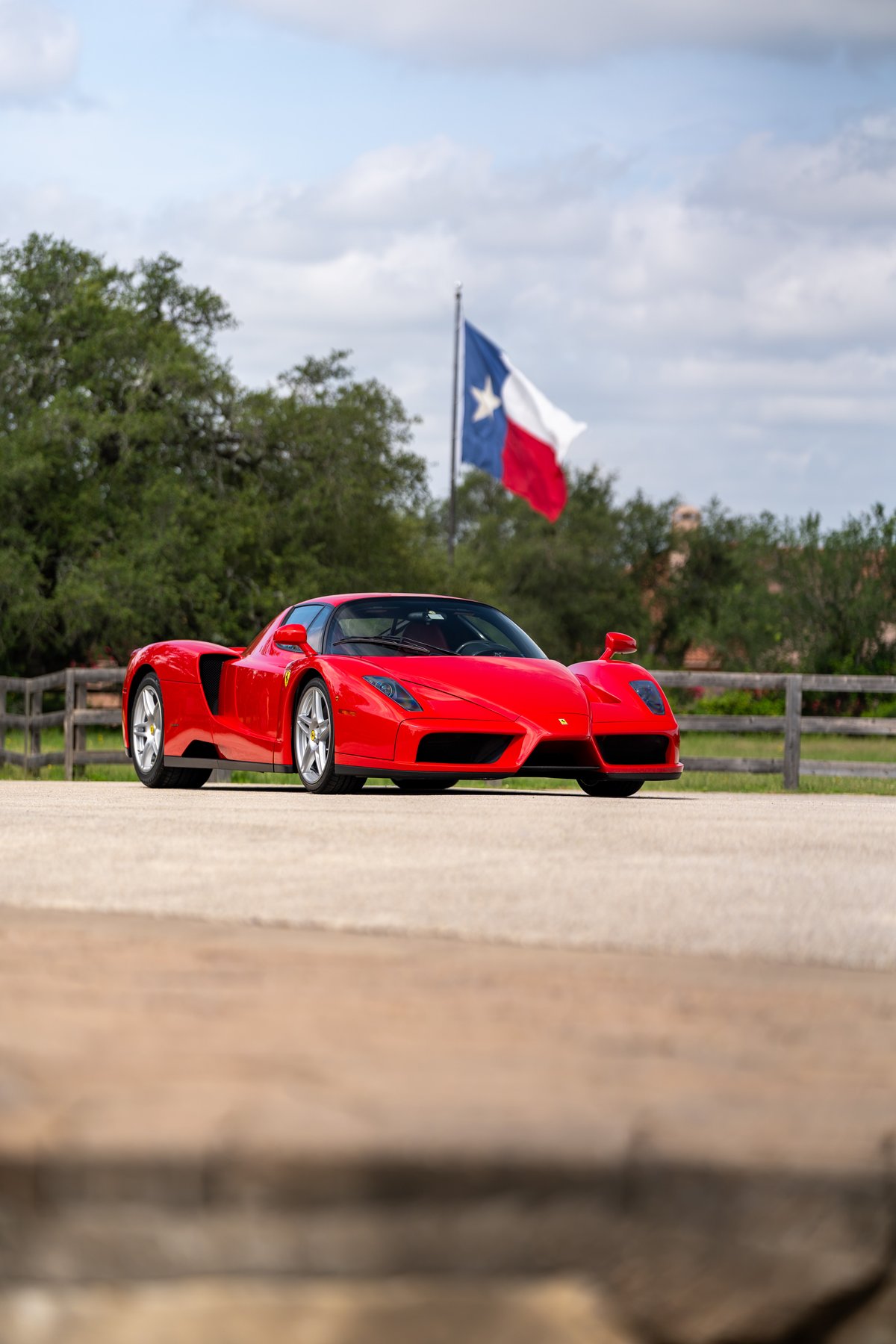 Rosso Corsa Ferrari Enzo with silver rims and a Texas flag in the background.