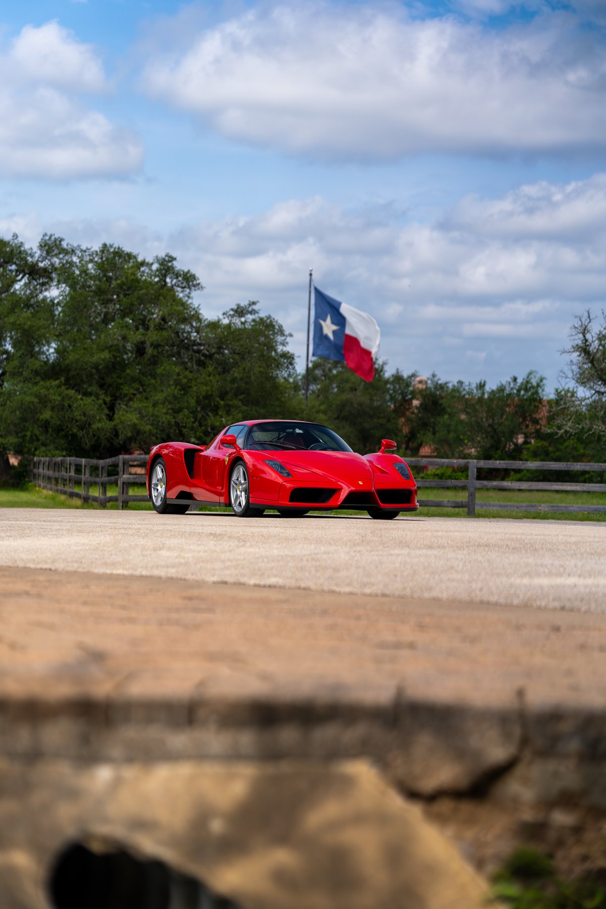 Red 2003 Ferrari Enzo with silver rims and a Texas flag flying in the background.