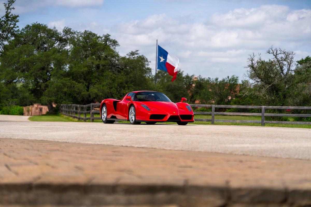 Red 2003 Ferrari Enzo supercar with silver rims drives on a Texas road.