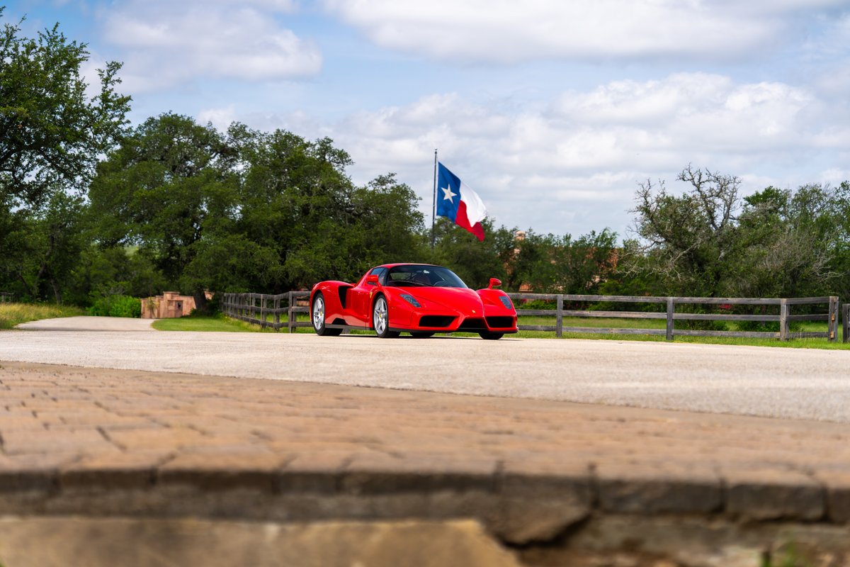 Rosso Corsa 2003 Ferrari Enzo, parked on a road with a Texas flag in the background.