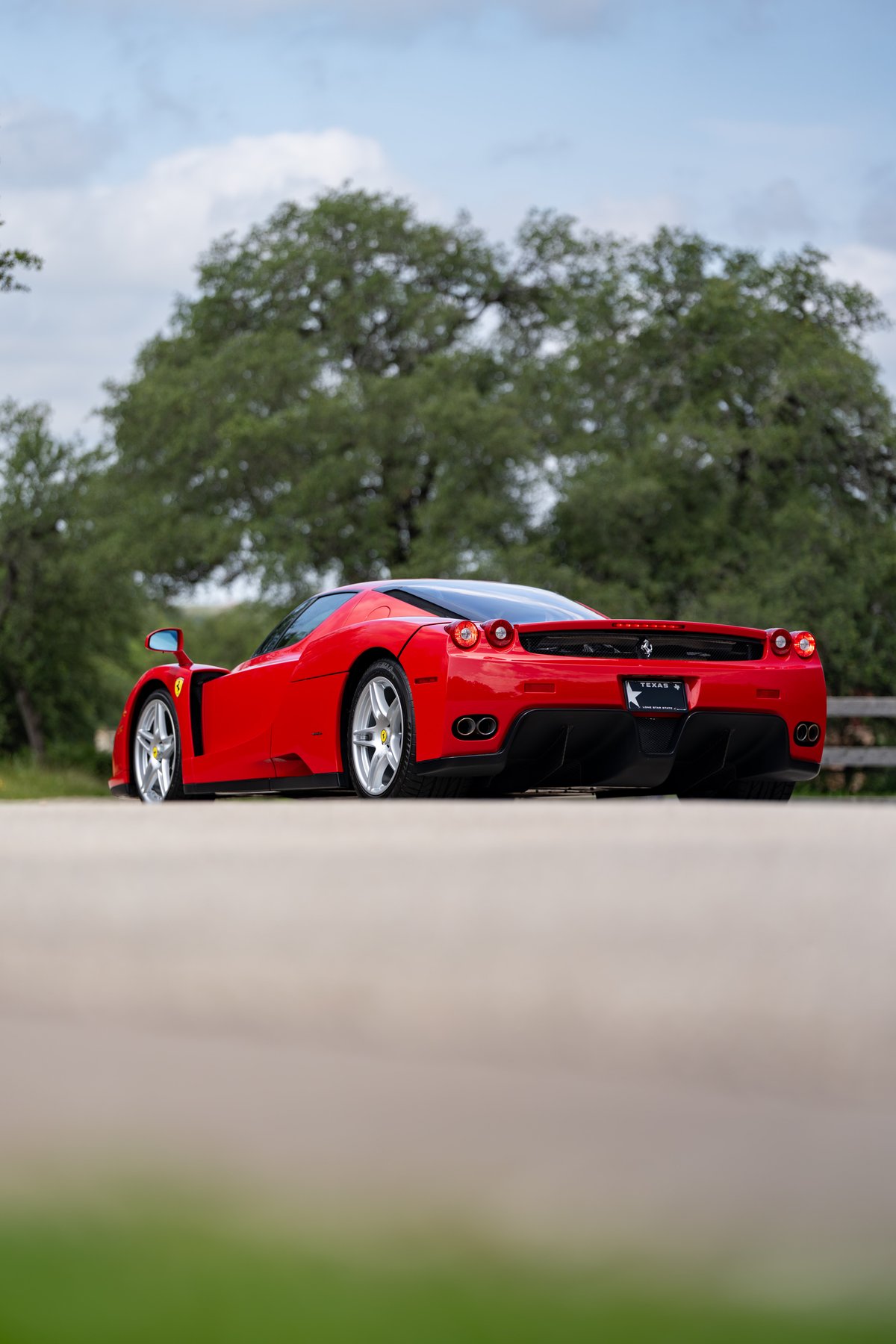 Rear view of a Rosso Corsa 2003 Ferrari Enzo with silver rims and quad exhaust pipes.
