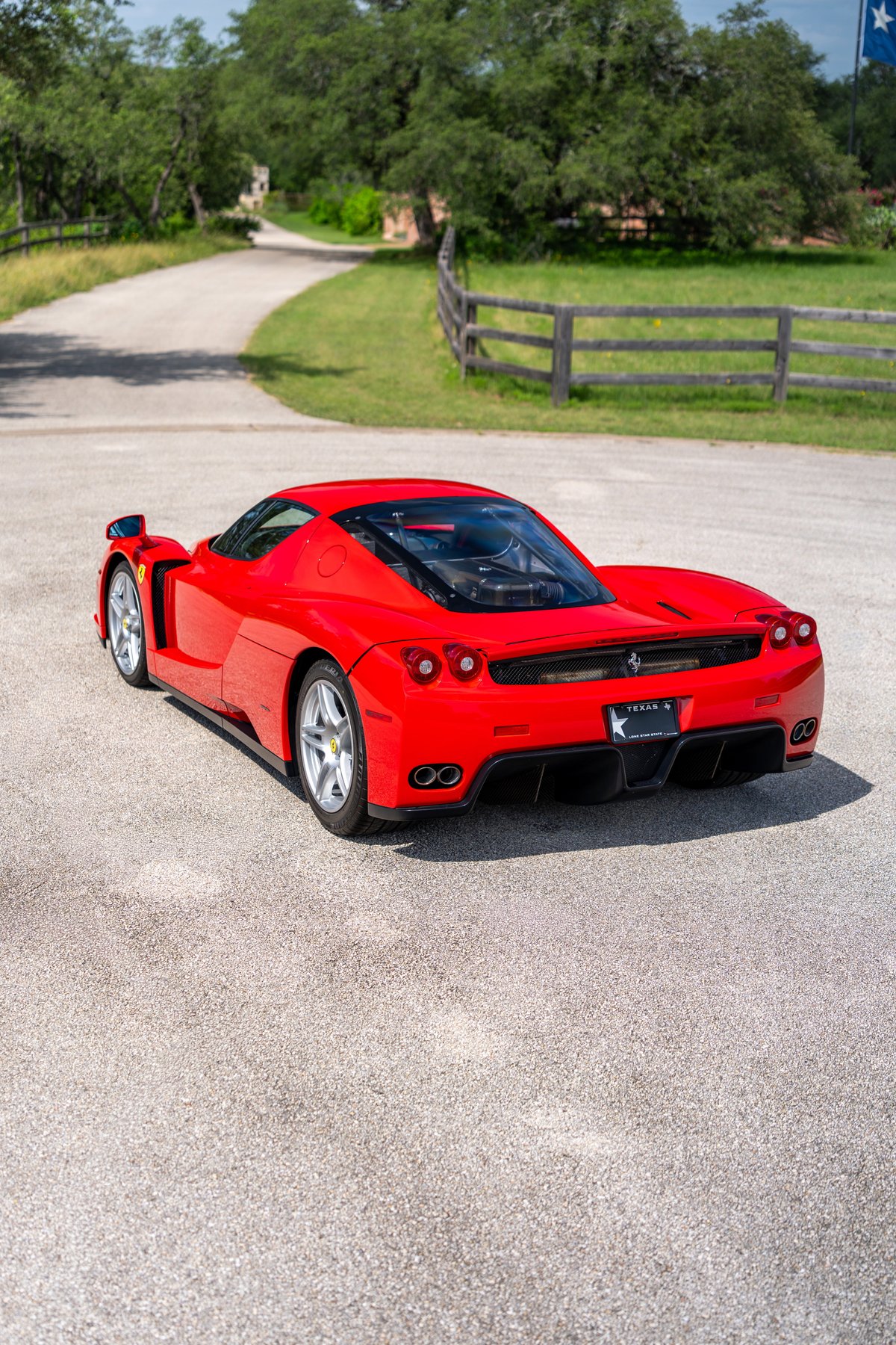 Rear view of a red 2003 Ferrari Enzo with silver rims and dual exhaust pipes.