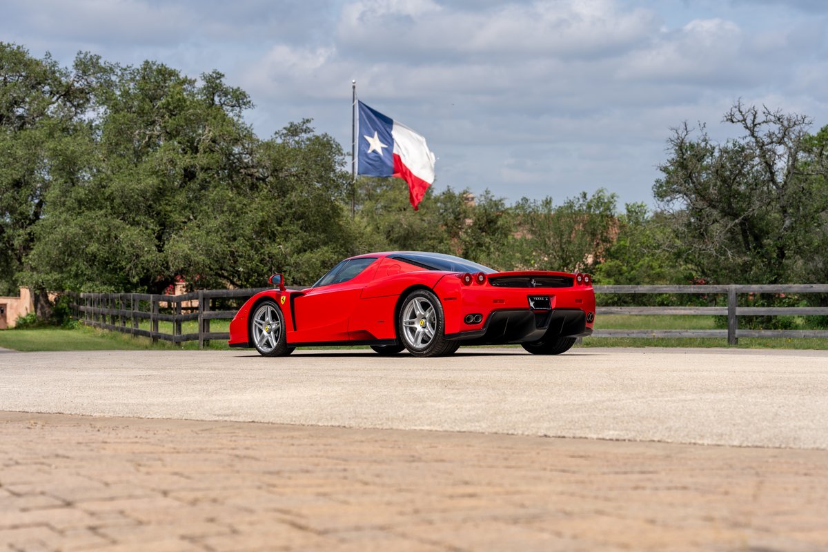 Red 2003 Ferrari Enzo with silver rims, parked outdoors near a Texas flag.