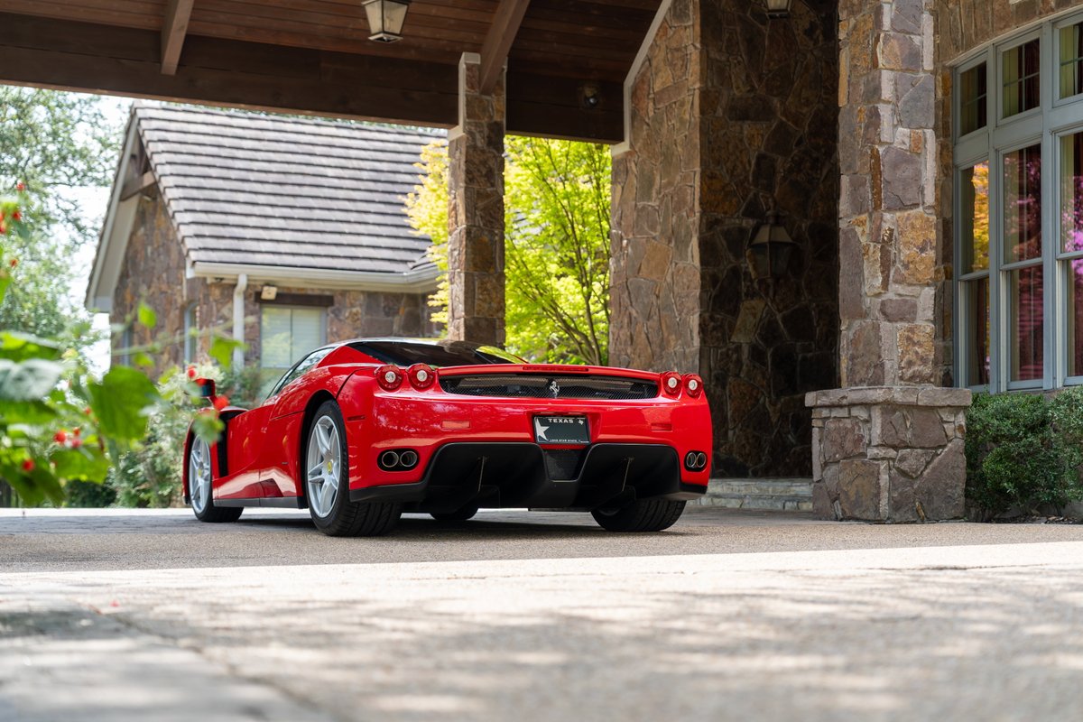 Red 2003 Ferrari Enzo with silver rims parked under a stone entryway.