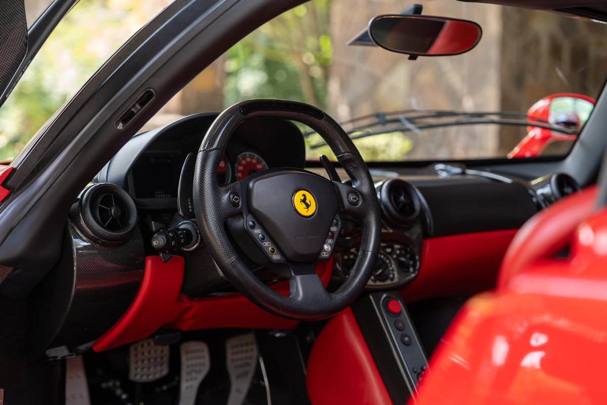 Interior of a red 2003 Ferrari Enzo, featuring a black steering wheel with the prancing horse logo and red trim.